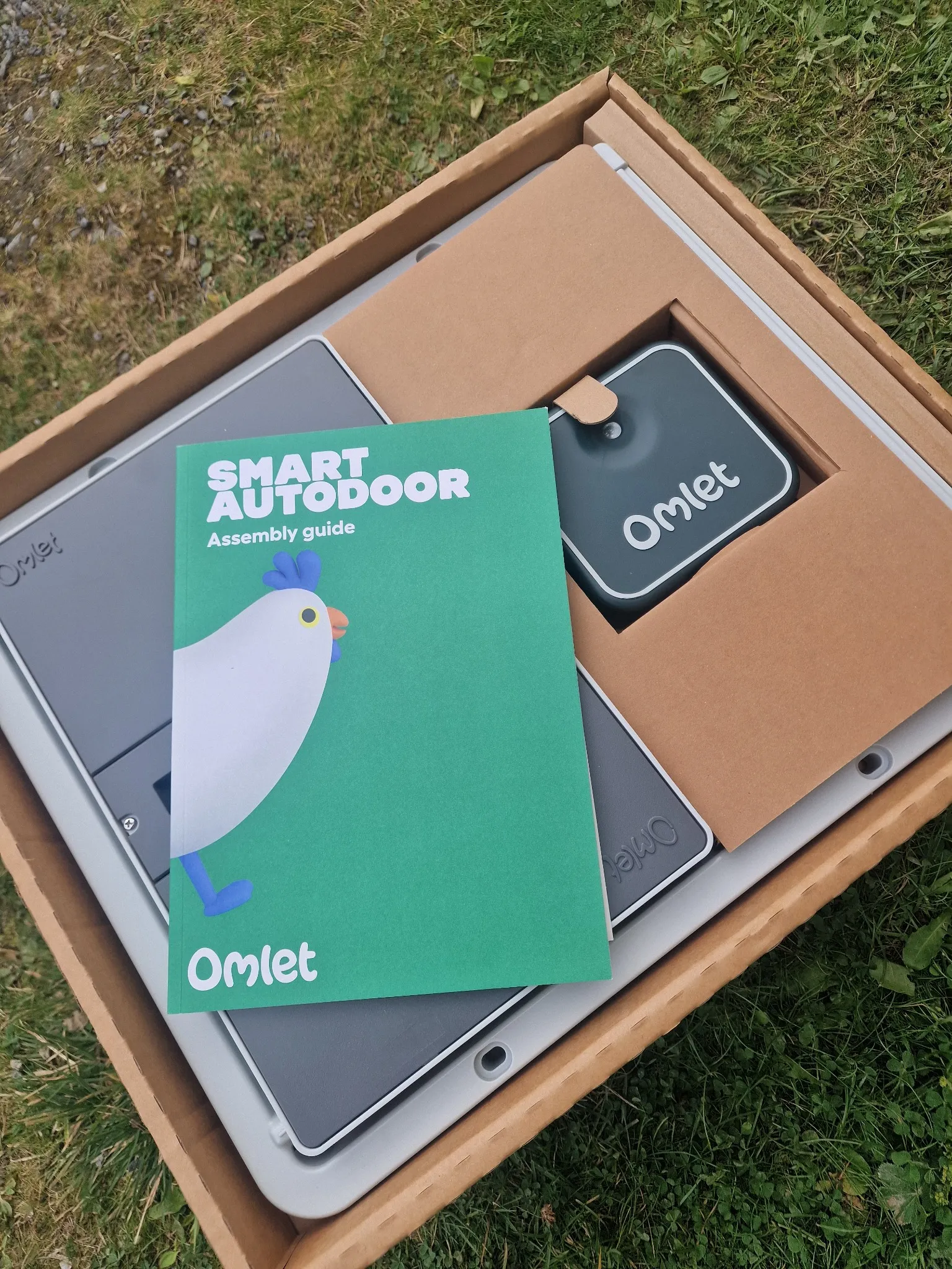Omlet Smart Autodoor in its box with the assembly guide on top.