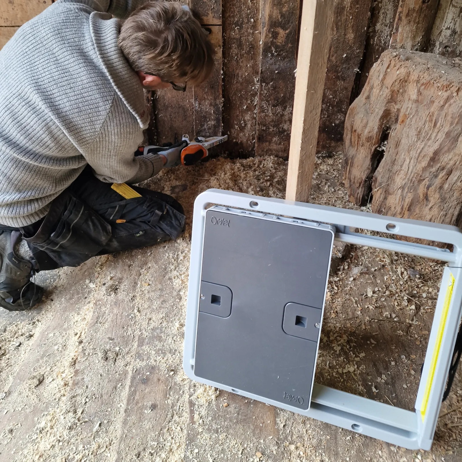 Man cutting the opening in the barn wall with a small electric chainsaw, with the door lying beside him.